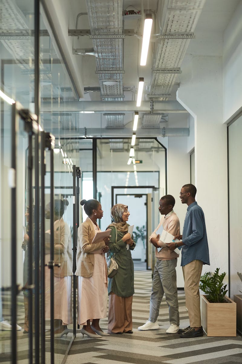 Four professionals engage in a friendly discussion in a modern office corridor.