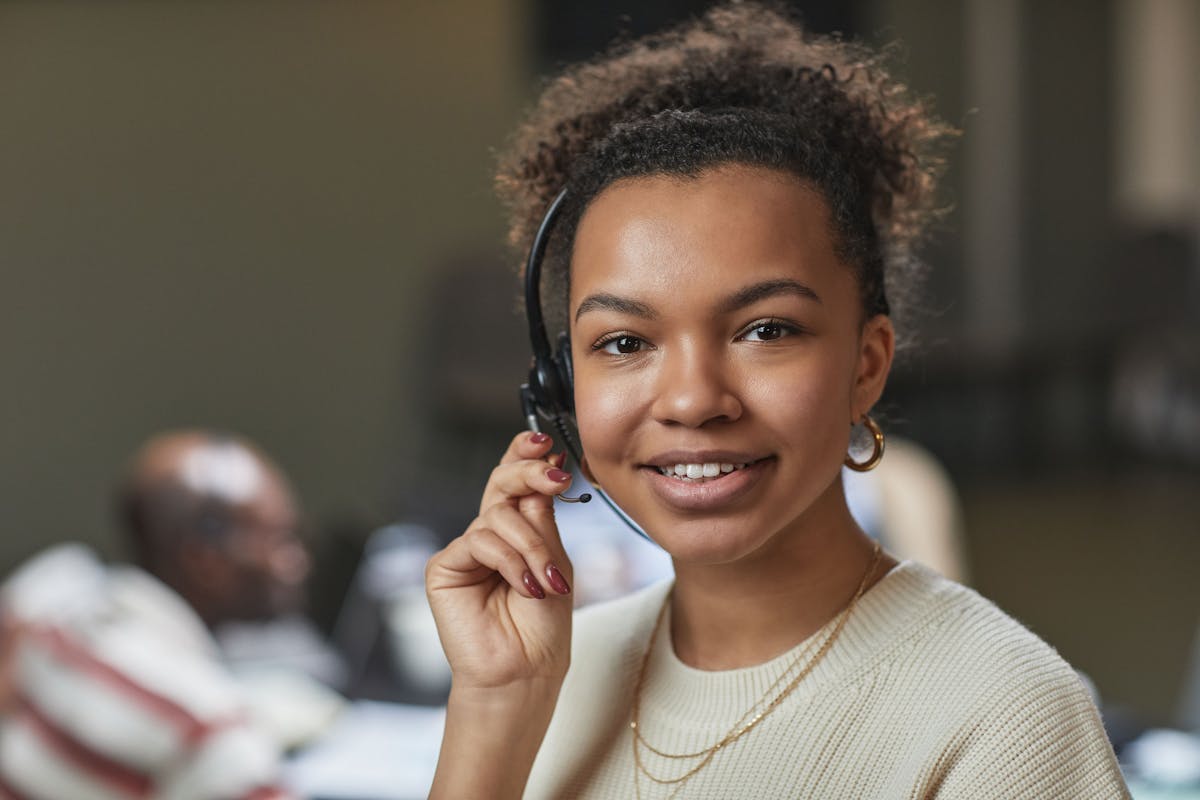 Friendly woman in a call center environment, wearing a headset and smiling.
