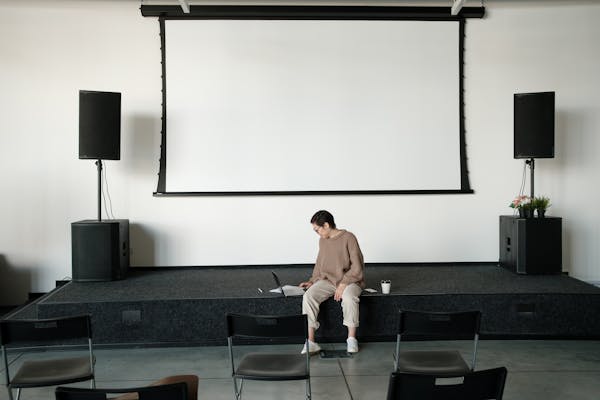 A solitary businesswoman using a laptop on stage in an empty conference room, symbolizing remote work.